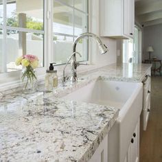 a kitchen with marble counter tops and white cabinets, along with a window over the sink