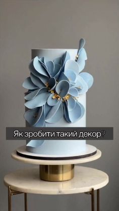 a three tiered cake with blue flowers on the top and gold trimmings