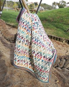 a blanket is hanging on a wooden stick in the dirt near some grass and trees