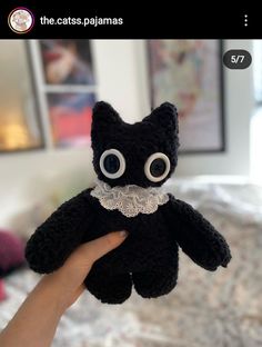 a hand holding a black stuffed animal with big eyes