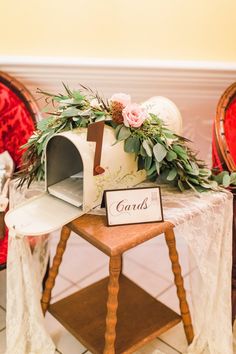 a table topped with flowers and mailbox on top of a wooden chair next to a white table cloth