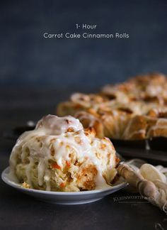 carrot cake cinnamon rolls with icing on a white plate next to a serving dish