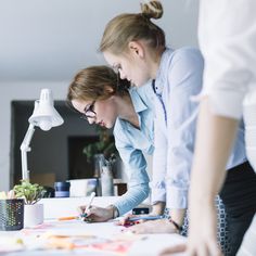 two women standing at a desk writing on paper