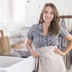 a woman standing in front of a kitchen sink with her hands on her hips and looking at the camera