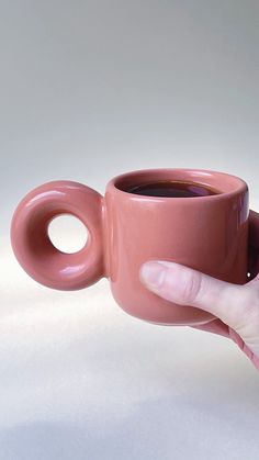 a person holding a pink coffee cup in their right hand and the other hand is pointing at it