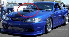 a blue car parked in a parking lot next to other cars with people standing around