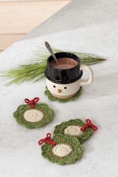 three crocheted coasters and a cup of tea on a table with pine needles