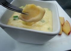 a spoon is being used to dip food in a white bowl with apples on the side