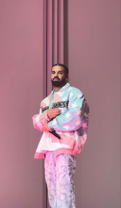 a man standing in front of a purple wall with his arms crossed