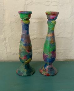 two colorful vases sitting next to each other on top of a green table with a white wall in the background