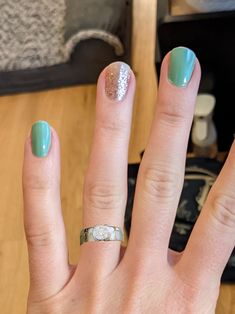 a woman's hand with green and silver nail polish on it, holding up her ring