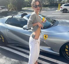 a woman standing next to a silver sports car