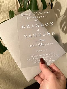 a person holding up a wedding card in front of a plant