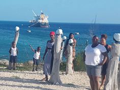 a group of people standing next to each other near the ocean with a ship in the background