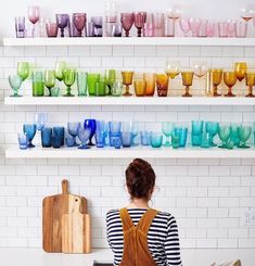 a woman standing in front of a shelf filled with cups and vases on it