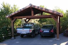 two pickup trucks parked under a wooden gazebo on a brick driveway with trees in the background