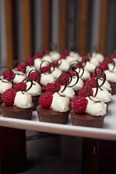 cupcakes with white frosting and raspberries are arranged on a table