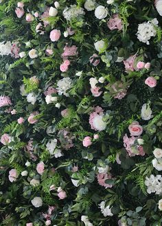 a wall covered in lots of pink and white flowers next to green leaves on top of it