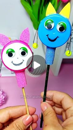 someone is holding two colorful paper faces on toothpicks in front of a pink table