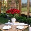 the table is set with two plates and a vase full of red flowers on it