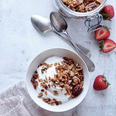 a bowl of yogurt and granola with strawberries next to it on a table