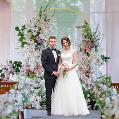 a bride and groom standing in front of a floral arch