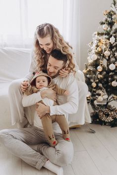 a man and woman holding a baby in front of a christmas tree with a small child