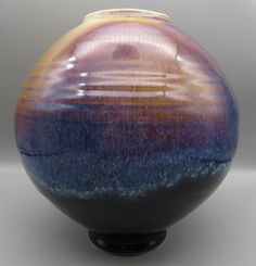 a black vase with blue, yellow and purple designs on the bottom is shown in front of a gray background