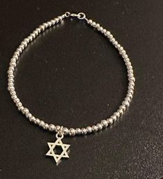 Embrace the beauty of Israeli craftsmanship with our exquisite Sterling Silver Beaded Star of David Bracelet. Skillfully handcrafted, this stunning piece features delicate sterling silver beads meticulously arranged to form the iconic Star of David, a powerful emblem representing Judaism and the rich heritage of Israel. Designed with an eye for detail, each bead reflects the brilliance of sterling silver, creating a captivating play of light as it gracefully adorns your wrist. The intricate inte Symbolic Star-shaped Adjustable Jewelry, Adjustable Symbolic Star Jewelry, Adjustable Star-shaped Symbolic Jewelry, Silver Beaded Bracelets With Star Charm, Silver Beaded Bracelet With Star Charm And Round Beads, Silver Hand-strung Charm Bracelet Gift, Adjustable Sterling Silver Star Bracelet, Silver Beaded Bracelet With Star Charm As Gift, Silver Beaded Bracelet With Star Charm For Gift