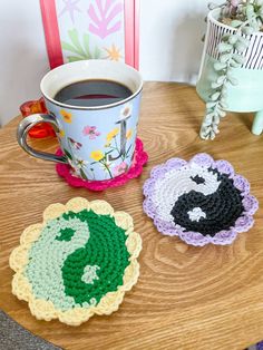 three crocheted coasters sitting on top of a table next to a cup of coffee