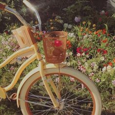 an old yellow bicycle with a basket on the front wheel and flowers in the background