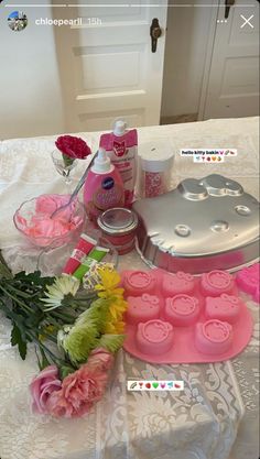 the table is covered with pink and white flowers, soaps, cupcake tins and other items