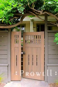 an open wooden door in front of a house with trees and bushes on either side