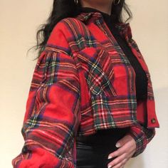 a woman with long black hair wearing a red plaid shirt and black leather pants, standing in front of a white wall