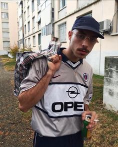 a man with a hat and glasses is holding a bottle in one hand and a backpack on the other