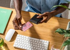 a person is holding a card near a keyboard and mouse on a wooden desk with plants