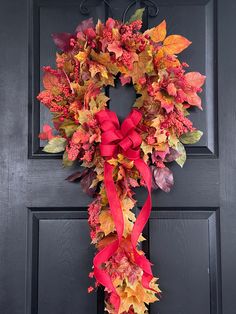 a wreath with red ribbon hanging on the front door decorated with autumn leaves and foliage