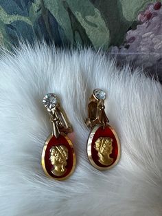 "Vintage 1960s - 70s red crystal clip-on dangle earrings with gold-tone Greek Goddess profile and clear crystal. These earrings are in excellent vintage condition. There are no missing elements are all original settings are in place and secure. Earring Details: * Clear round crystals * Gold-tone metal that forms figure in profile with red backdrop * Original clip back * Measures 1.5\" long and 0.5\" wide ALL SALES ARE FINAL. Unless otherwise stated all vintage items are used and may have minor t Vintage Red Clip-on Earrings For Anniversary, Vintage Red Drop Clip-on Earrings, Vintage Gold-plated Clip-on Earrings, Red Vintage Clip-on Earrings, Vintage Yellow Gold Clip-on Earrings, 60s Jewelry, Red Backdrop, Blue Crystal Earrings, Red Crystals