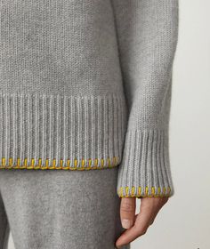 a close up of a person wearing a gray sweater and pants with yellow trims