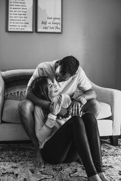 a man and woman sitting on top of a couch with their arms around each other