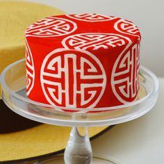 a red and white cake on a clear platter with yellow hats in the background