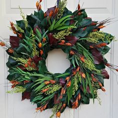 a wreath hanging on the front door of a house with leaves and flowers around it