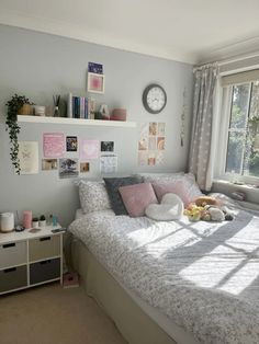 a bed with pillows and stuffed animals on it in a bedroom next to a window