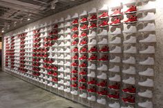 a large display of red and white shoes on a wall in an office building with concrete flooring