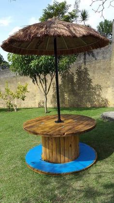 an umbrella sitting on top of a wooden table in the middle of some grass with a blue mat underneath it