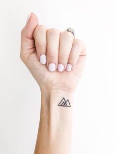 a woman's hand with a small triangle tattoo on her left wrist and the other arm