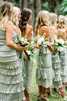 a group of women standing next to each other holding bouquets in their hands and wearing dresses