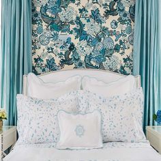 a bed with blue and white floral wallpaper next to a curtained headboard