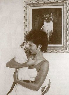 a woman holding a cat in front of a painting with a cat on the wall