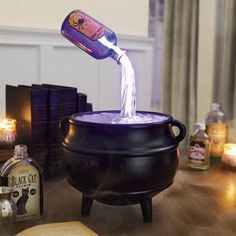 a bottle is pouring into a caulder on a table with books and candles